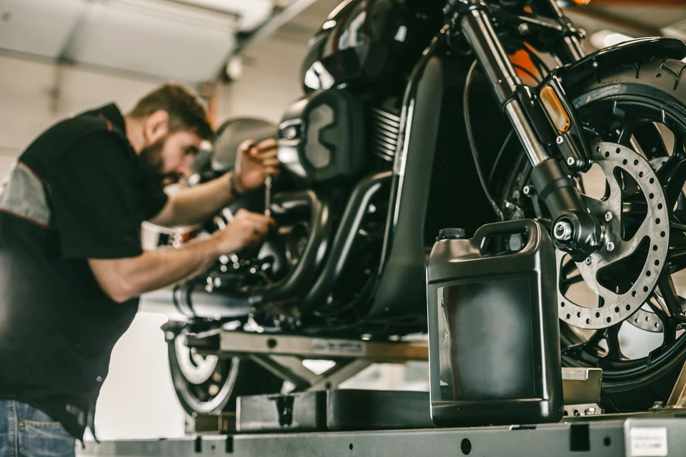 Atelier de r&eacute;paration moto en int&eacute;rieur, m&eacute;canicien barbu concentr&eacute; travaillant sur une moto noire sur&eacute;lev&eacute;e