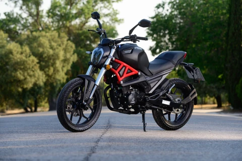 Un homme barbu en chemise à carreaux rouge et bleu travaille à l'extérieur sur une moto, vapeur visible suggérant un travail mécanique en cours