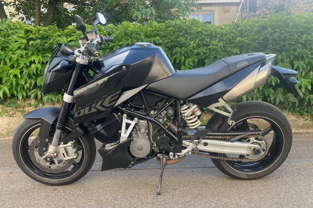 Moto sportive noire stationnée sur route goudronnée, entourée de végétation verte luxuriante