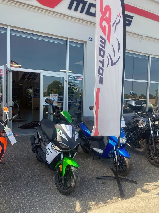 Atelier de r&eacute;paration moto avec m&eacute;canicien en salopette bleue travaillant sur une moto verte et noire