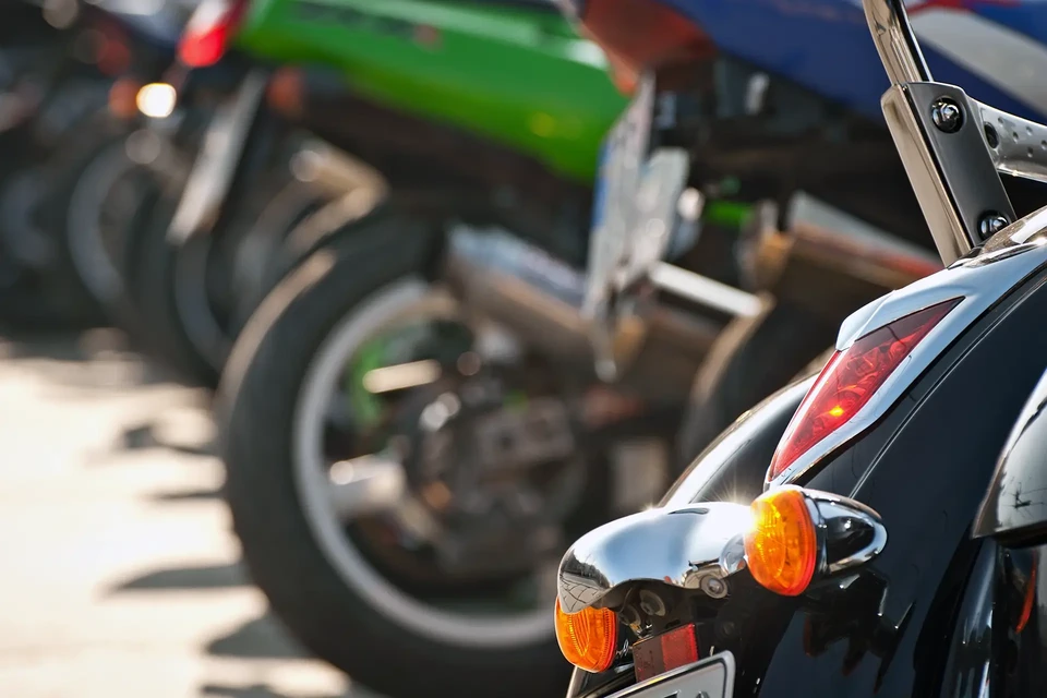 Scène extérieure urbaine avec moto touring stationnée sur pavés, devant espaces verts et immeuble résidentiel en arrière-plan