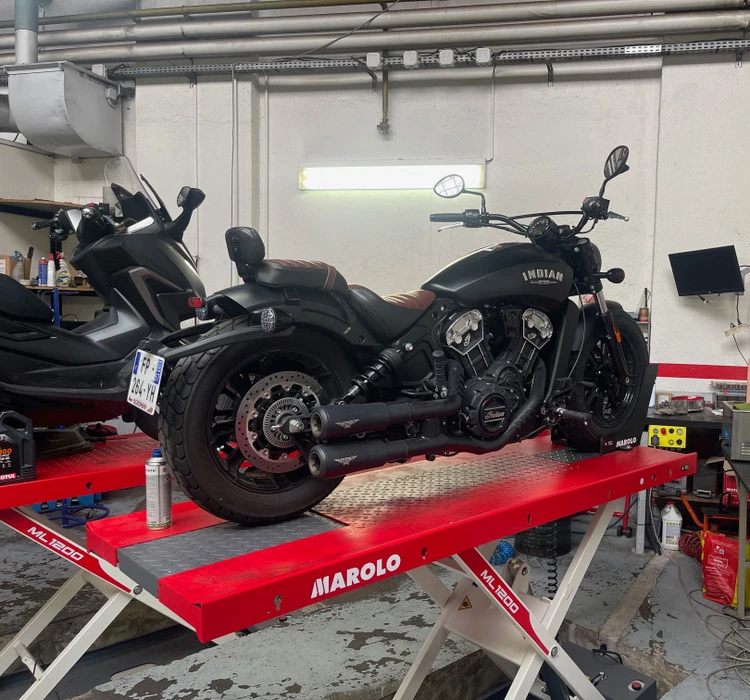 Atelier de réparation moto avec mécanicien travaillant sur une moto sportive surélevée sur pont élévateur rouge Marolo