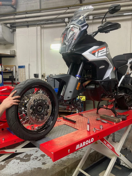 Atelier de réparation moto avec mécanicien travaillant sur une moto adventure touring noire et grise