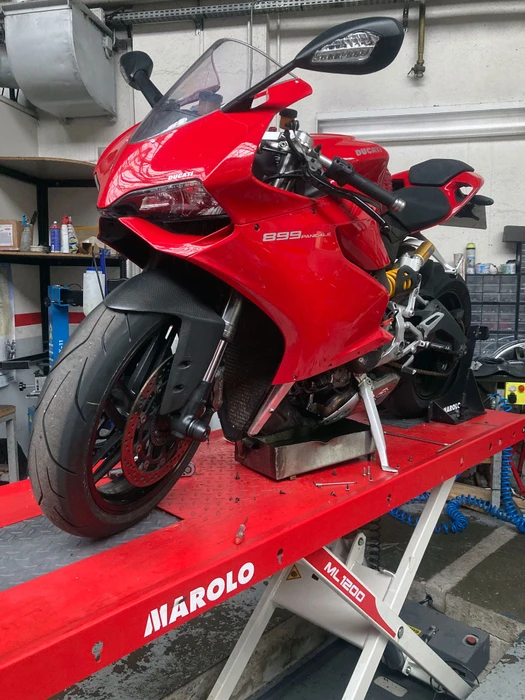 Scène extérieure avec moto sportive noire garée sur route goudronnée, végétation verte dense en arrière-plan, éclairage naturel diurne