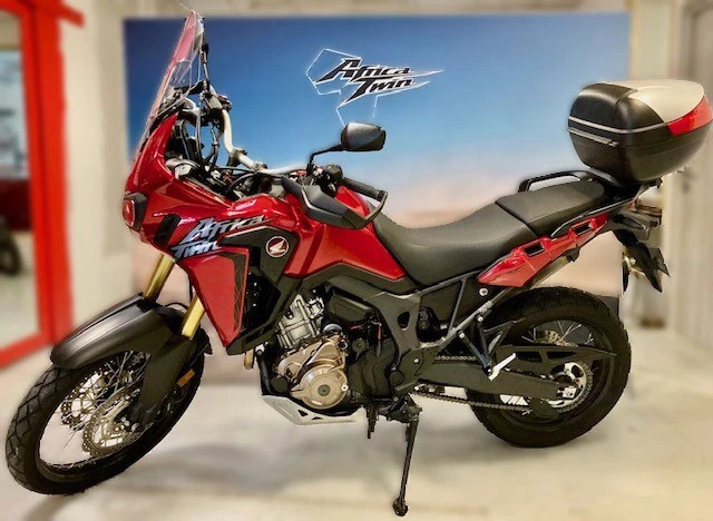 Scène extérieure avec moto sportive noire garée sur route goudronnée, végétation verte dense en arrière-plan, éclairage naturel diurne